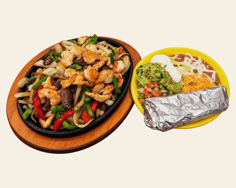 Combo fajitas on a sizzling skillet with rice, beans, guacamole and tortillas