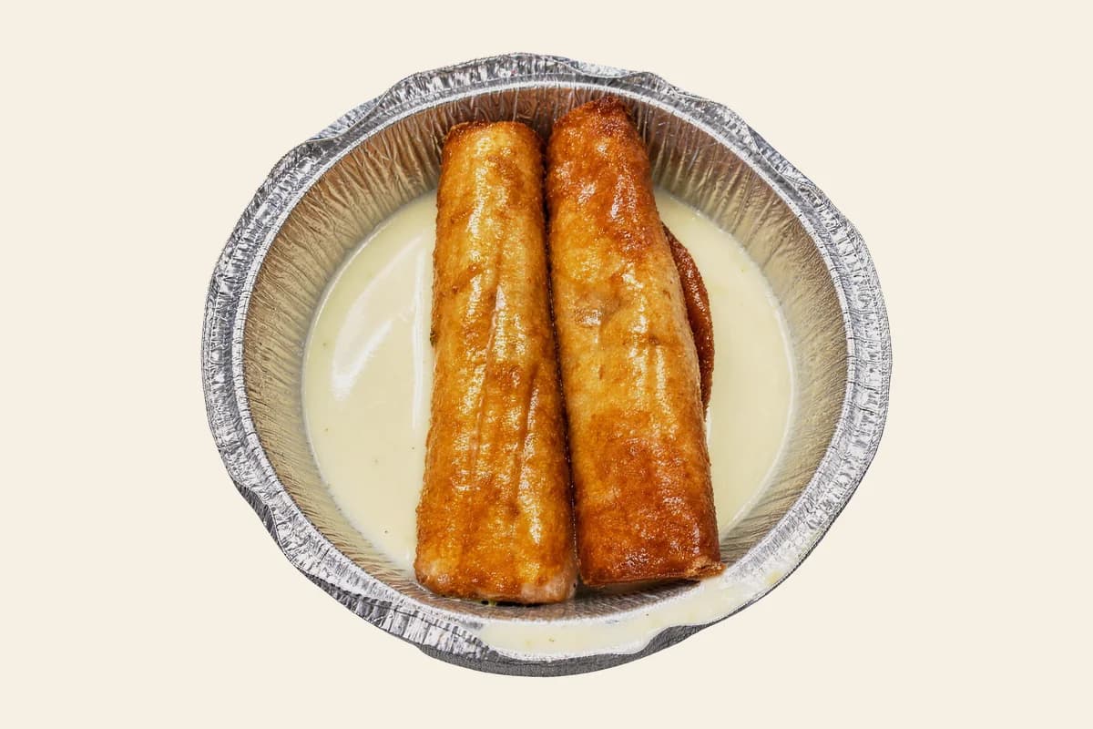 Two especial flautas resting in white cheese sauce in a foil tray