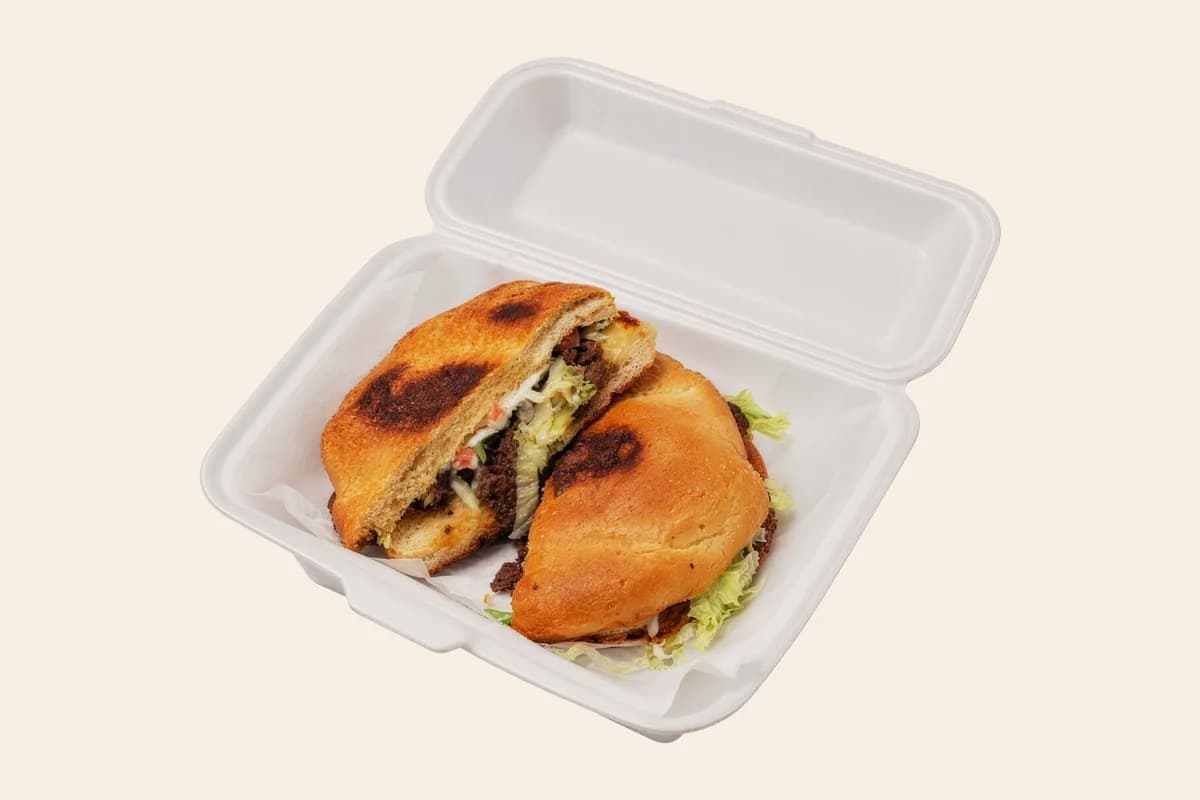 A Mexican torta cut in half on grilled bread in a takeout box